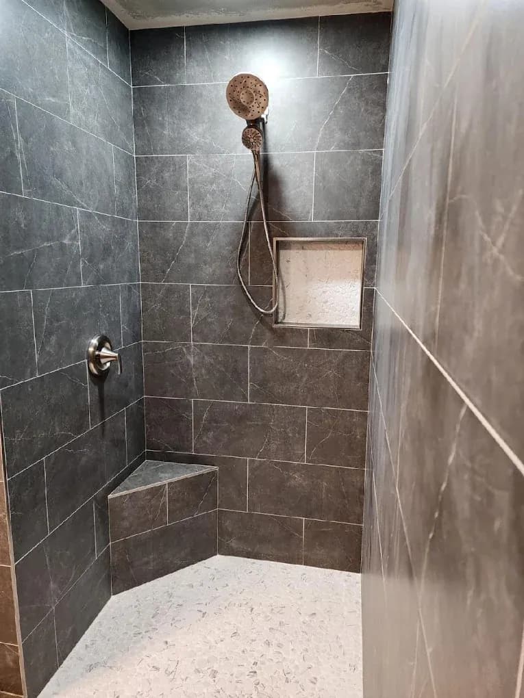 A dark gray stone tile shower with built-in corner seat and caddy.