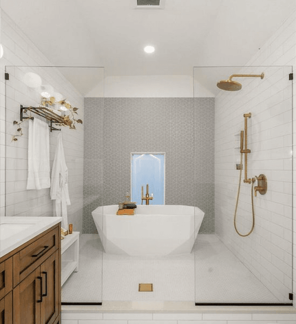 A white and gray bathroom with a walk-in shower with gold-colored fixtures, and a large soaking bathtub in the center.