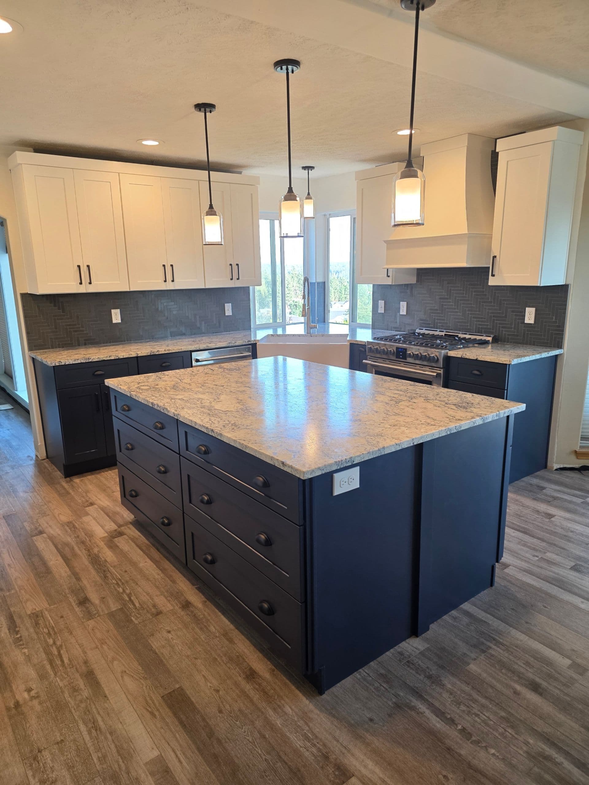 A kitchen with white upper cabinets and dark-colored lower cabinets, large central island, and white and gray marbled countertops.