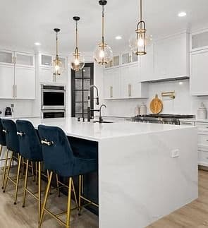 A kitchen with white cabinets and large white stone waterfall island with navy blue bar stool seating.